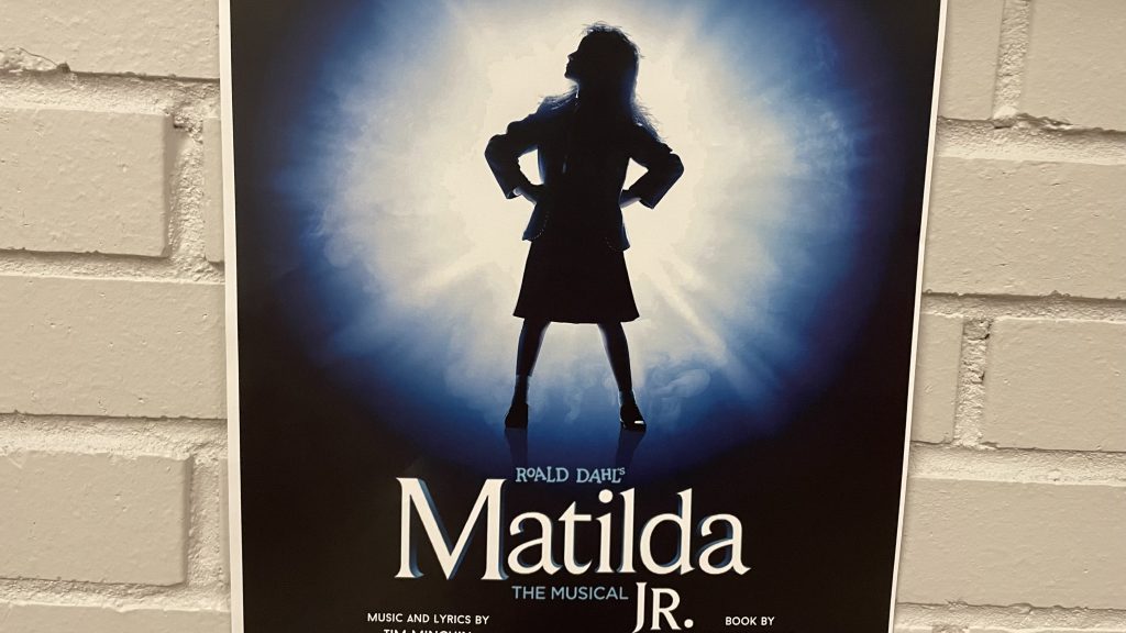 Poster for Matilda The Musical Junior on a brick wall painted white.