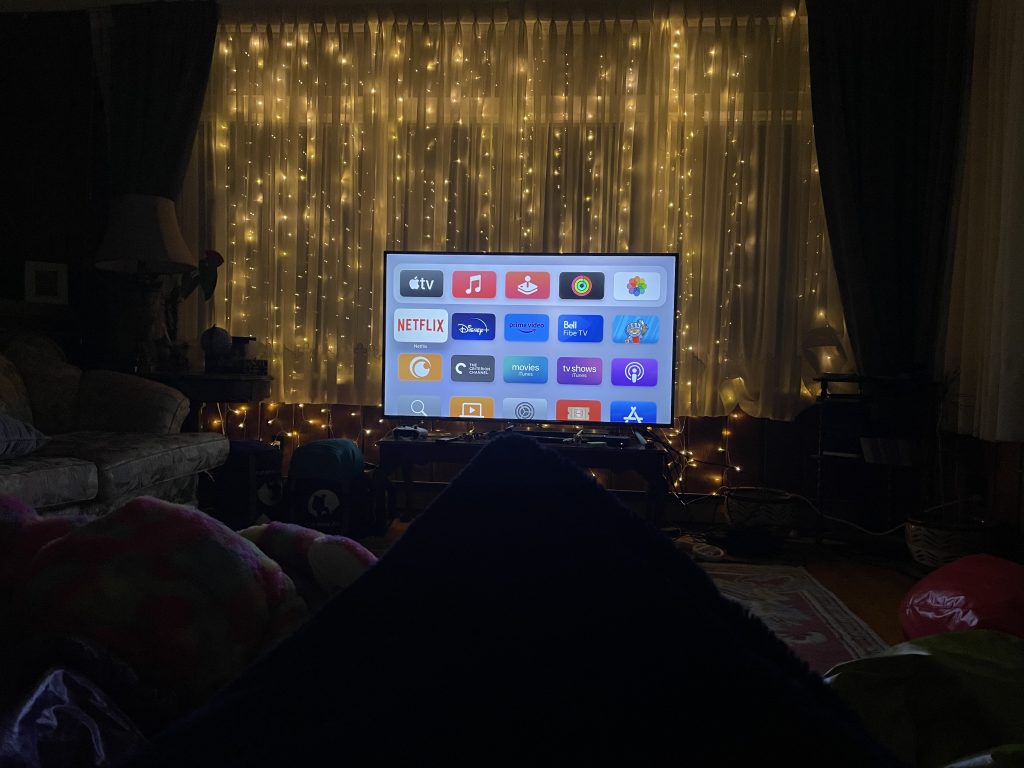 A night shot of a TV in front of a huge window with strings of small lights behind a sheer curtain, creating a relaxing glow.